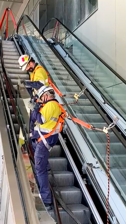Two Men working on escalator attached to temporary fall restraint line Close-up